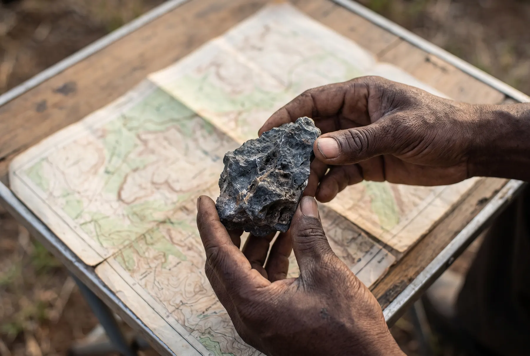 Hands holding a rock sample above an unreadable map.